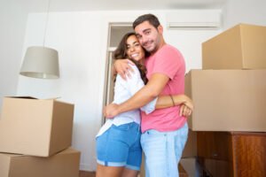 Casal feliz se mudando para um novo apartamento, parado entre caixas de papelão e se abraçando